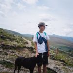 Teenager hiking a mountain trail with his dog trotting alongside