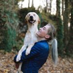 woman carrying her tan dog in her arms