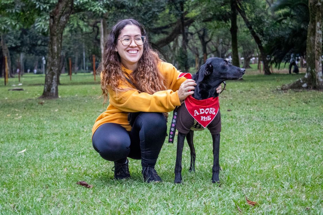 woman smiling with an adoptable black dog in a park