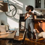 woman drinking coffee in a kitchen while her dog sits at her feet