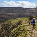 A hiker walking with her dog on a rocky mountain trail