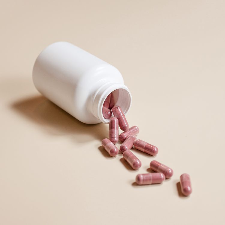 capsules spilling from a white medicine bottle on a beige surface