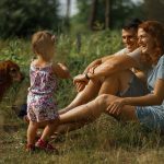 family with a baby and their dog relaxing together on the grass