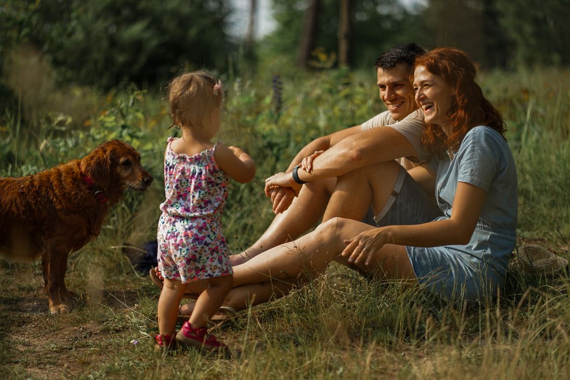 family with a baby and their dog relaxing together on the grass